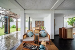 Un salon moderne avec un plafond en bois, un ensemble de canapés agrémentés de coussins, une table basse et une vue sur l’extérieur.
