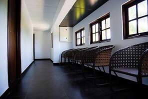 A hallway with a row of wicker chairs, a dark floor, and windows with blinds.