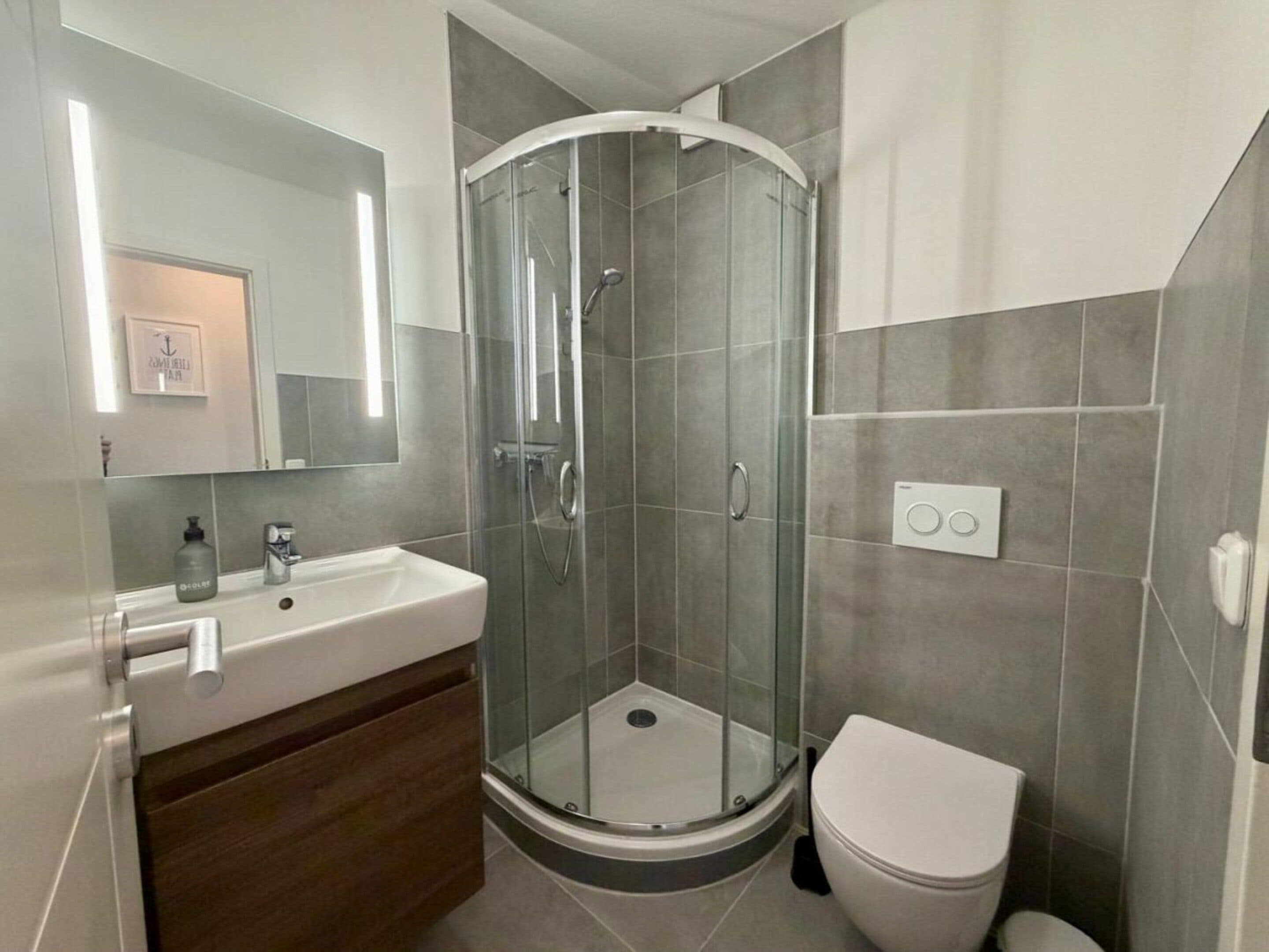 A bathroom with a glass-enclosed shower, a white sink, a toilet, and a mirror.