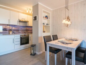 A modern kitchen with white cabinets, a built-in oven, and a dining table with chairs. - Utholm 5a - Kleine Brise (St. Peter-Ording)