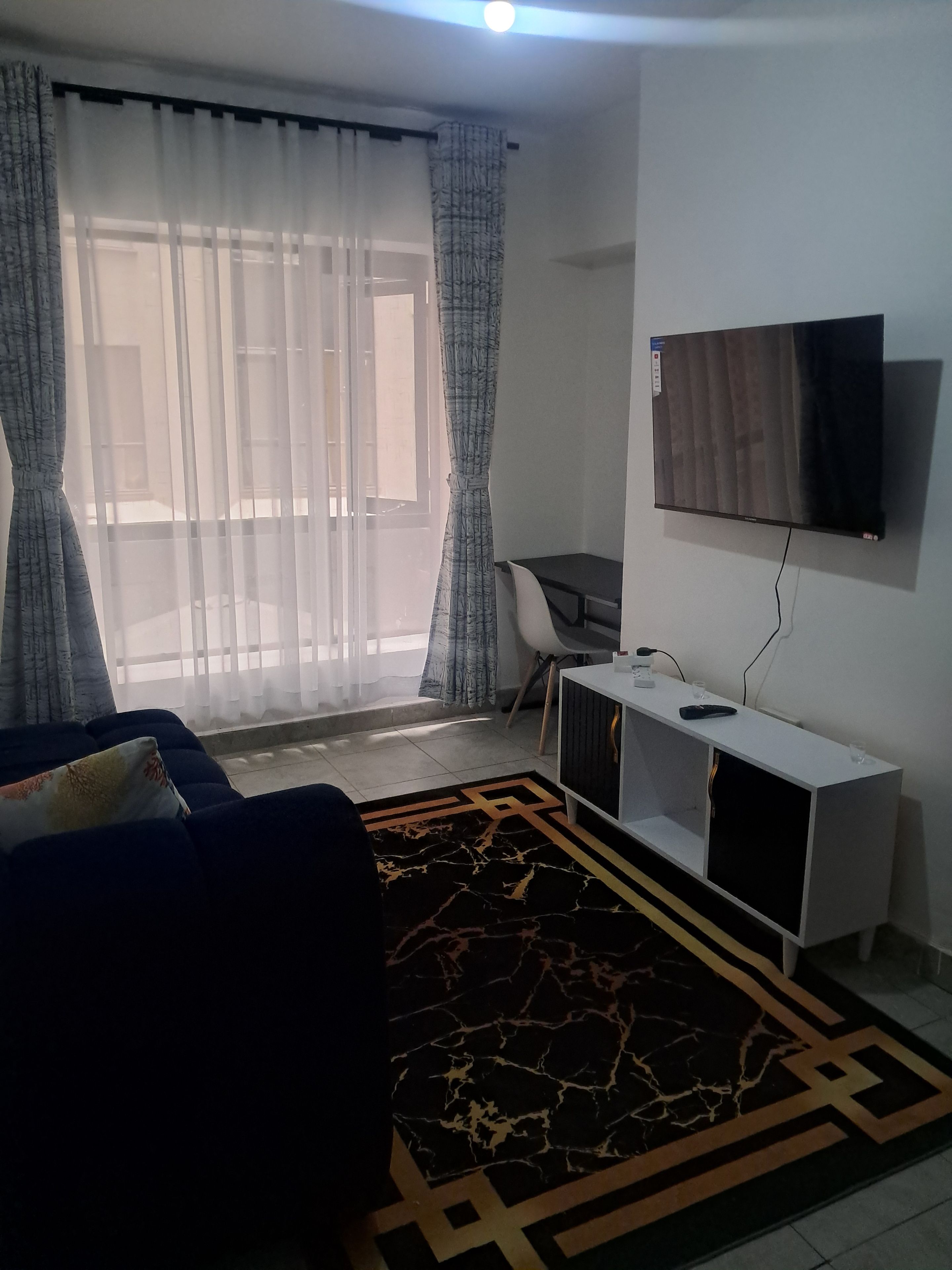 Una sala de estar con un sofá, un televisor montado en la pared, un escritorio y una alfombra estampada.