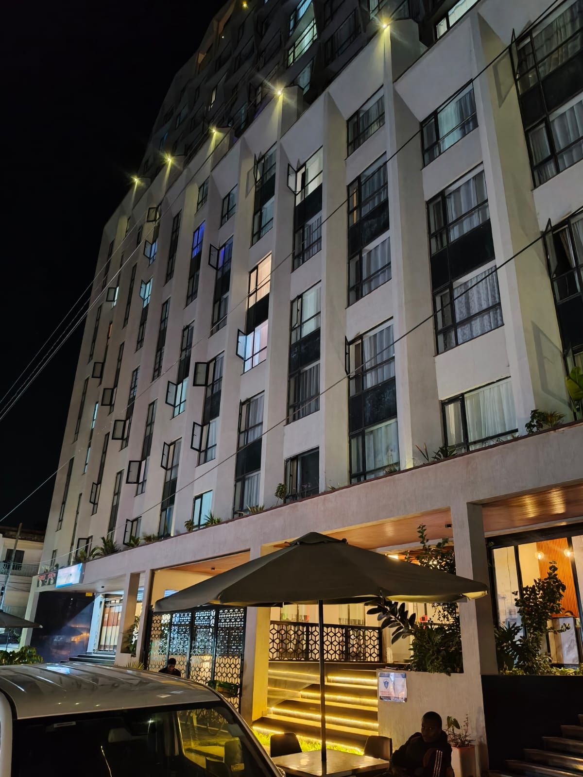 A multi-story hotel with a modern facade, a covered entrance area with seating, and a staircase leading to the entrance.