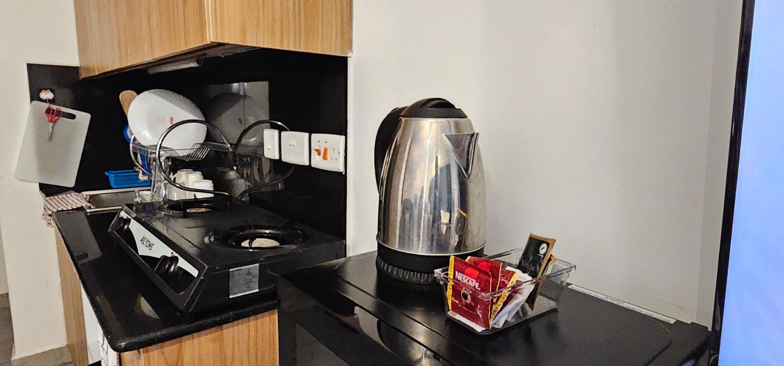 Une petite cuisine équipée d’une cuisinière, d’une bouilloire et d’un panier de sachets de café Nescafé.