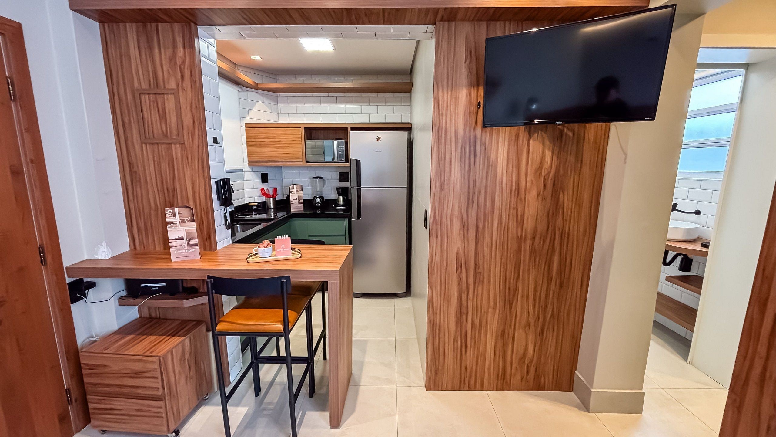Una cocina compacta con comedor, un refrigerador empotrado y un televisor de pantalla plana montado en la pared.