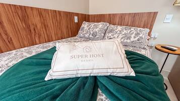 Una cama bien hecha con una colcha verde, un almohadón con el texto 'SUPER HOST BRASIL' y un cabecero de madera.