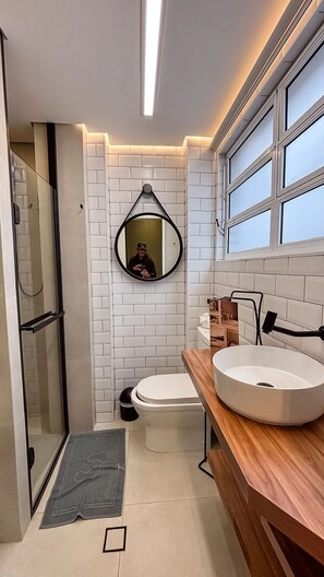 Ein modernes Badezimmer mit einer Duschkabine aus Glas, einer Toilette, einem Waschbecken mit Holzablage und einem Spiegel an der Wand.