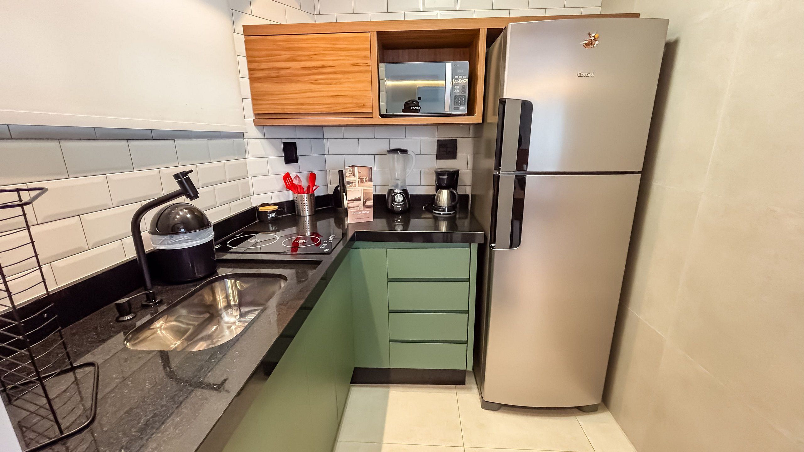 A compact kitchen with a stainless steel refrigerator, a kettle, a coffee maker, and a microwave.