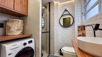 Uma casa de banho compacta com máquina de lavar roupa, sanita, espelho e lavatório.
