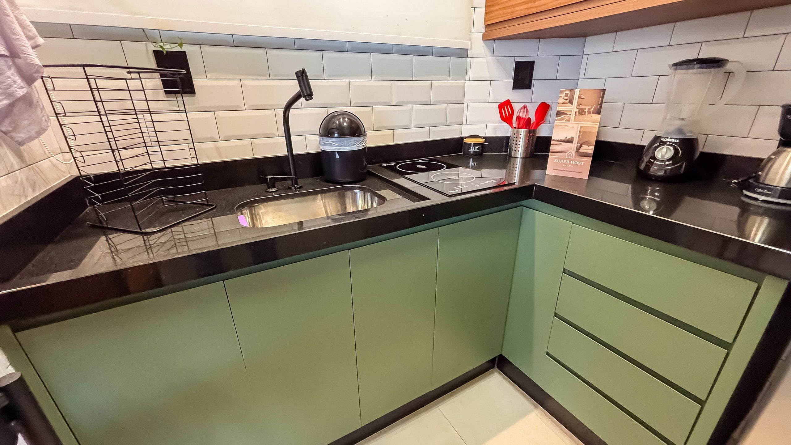 A modern kitchen with a black countertop, stainless steel sink, and green cabinets.
