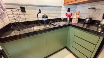 A modern kitchen with a black countertop, stainless steel sink, and green cabinets.