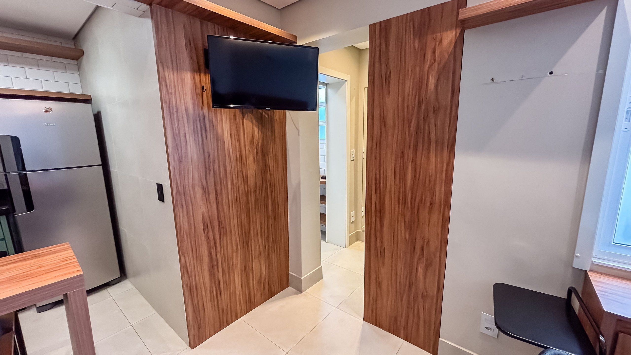 Una cocina moderna con refrigerador empotrado y un televisor de pantalla plana montado en una pared de madera.