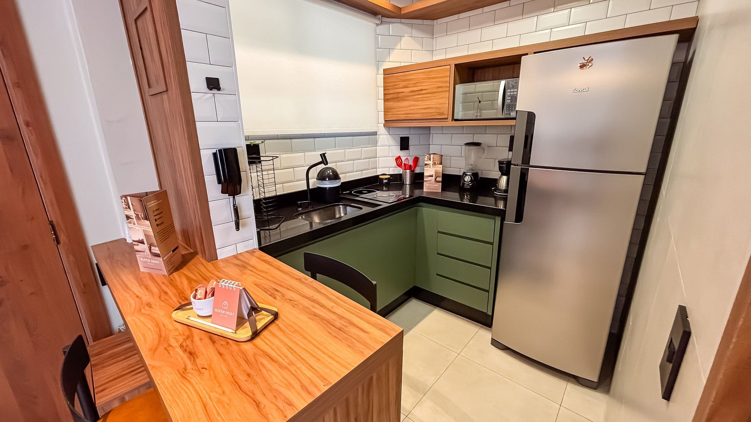 A compact kitchen with a built-in microwave, a stainless steel refrigerator, and a wooden dining table with a tray.