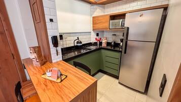 A compact kitchen with a built-in microwave, a stainless steel refrigerator, and a wooden dining table with a tray.