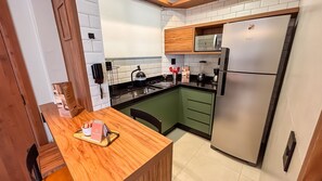 Una cocina compacta con microondas integrado, refrigerador de acero inoxidable y una mesa de comedor de madera con una bandeja.
