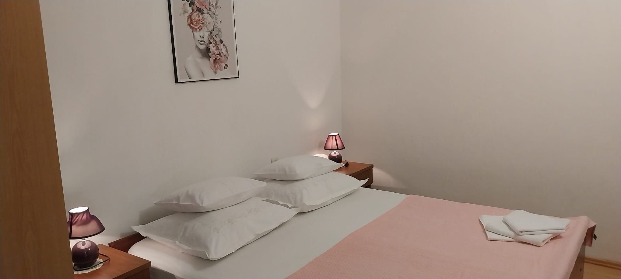 A bedroom with a bed, pillows, a bedside table with a lamp, and a wall-mounted picture.