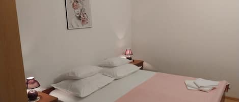 A bedroom with a bed, pillows, a bedside table with a lamp, and a wall-mounted picture.