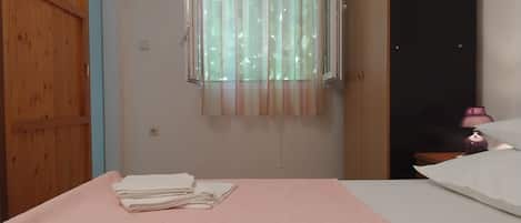 A room with a bed, a window with curtains, a door, and a nightstand with a lamp.