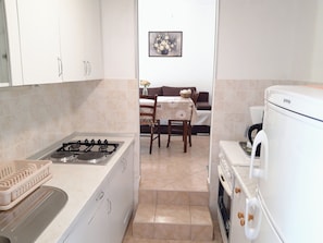 A compact kitchen with a gas stove, a white refrigerator, and a dining area with a table and chairs. - Kuča na rjeci s velikim vrtom I pogledom na planinu, 3 km.od mora-Split 10km. (Žrnovnica)