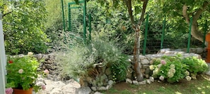 A garden with a stone wall, various plants, and a green trellis structure. - Kuča na rjeci s velikim vrtom I pogledom na planinu, 3 km.od mora-Split 10km. (Žrnovnica)
