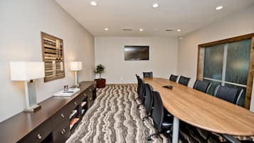 A conference room with a long table, chairs, a desk with a lamp, a potted plant, and a painting on the wall.