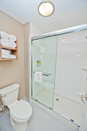 A modern bathroom with a glass-enclosed shower, a toilet, and a shelf with neatly folded towels. - Free Breakfast! 2BR Suite + Outdoor Pool Access (Humble)