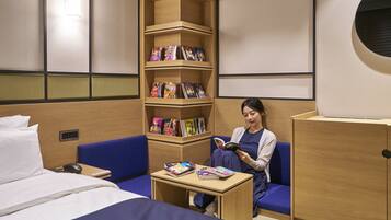 Una habitación con una cama, un sofá azul, una pequeña mesa con libros y una estantería llena de libros de colores.