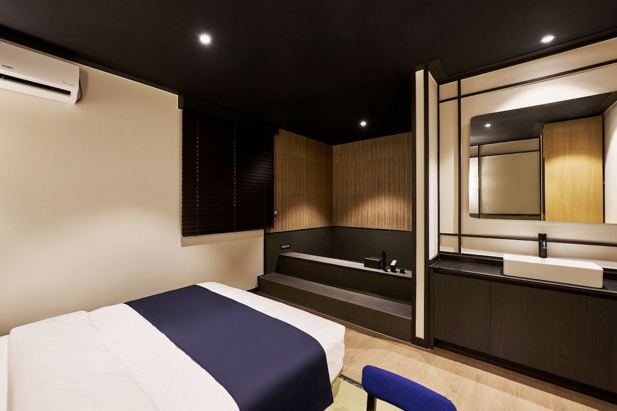 Una habitación de hotel moderna con cama, un banco integrado, un espejo grande y una bañera.