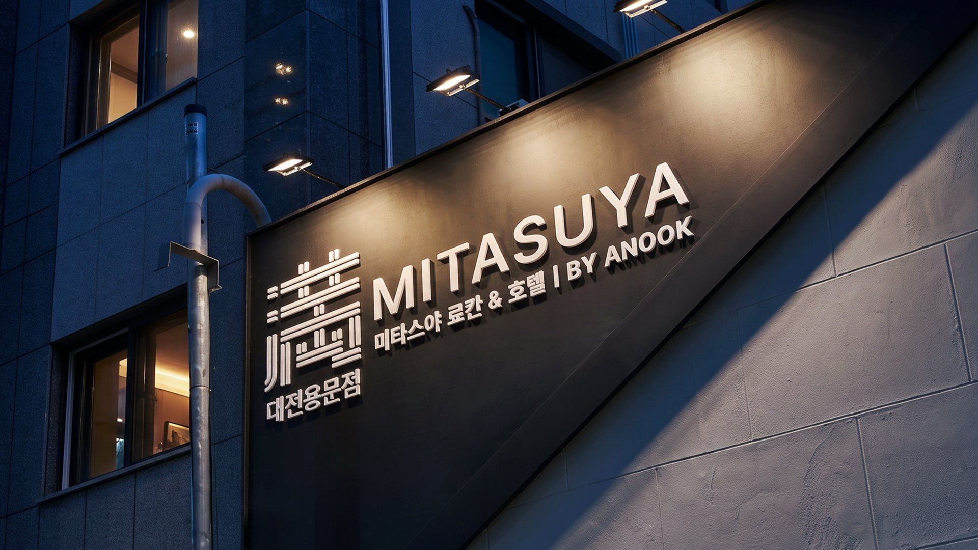 Fachada de edificio con señalización iluminada de 'MITASUYA BY ANDOOK' en inglés y coreano.