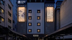 Exterior del Ryokan & Hotel Mitsuya, con fachada moderna, entrada central, amplias ventanas y señalización iluminada.
