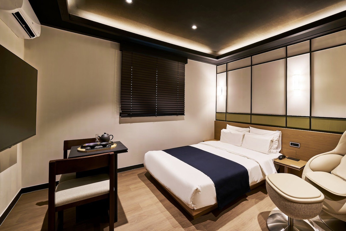 Una habitación de hotel con cama, mesita de noche, silla y escritorio con juego de té.