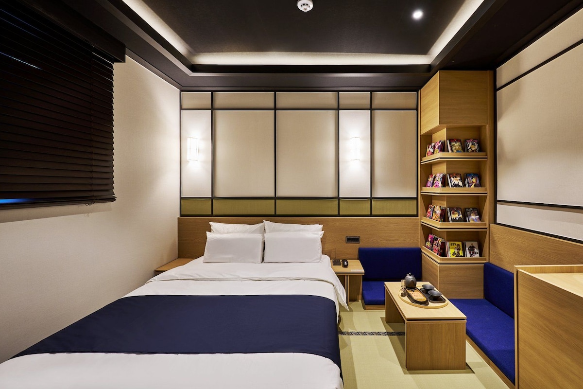 Habitación de hotel con cama, escritorio, estantería y zona de estar.