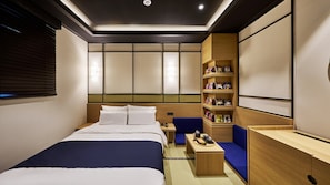 Habitación de hotel con cama, escritorio, estantería y zona de estar.