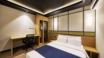 A hotel room with a bed, desk, chair, and a wardrobe.