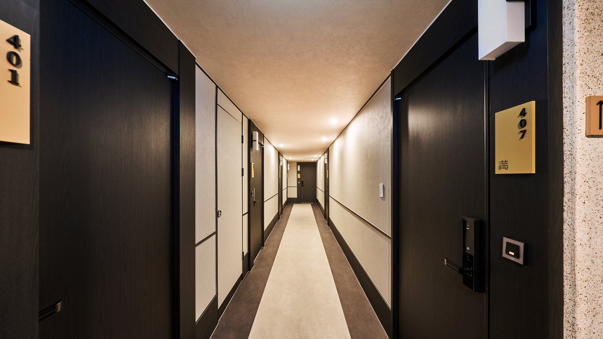 Un pasillo de hotel con puertas numeradas 401 y 407, suelo alfombrado y techo de color claro.