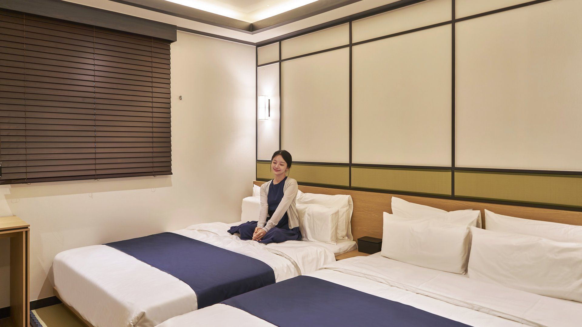 Habitación de hotel con dos camas, una mesita de noche y una ventana con persianas.