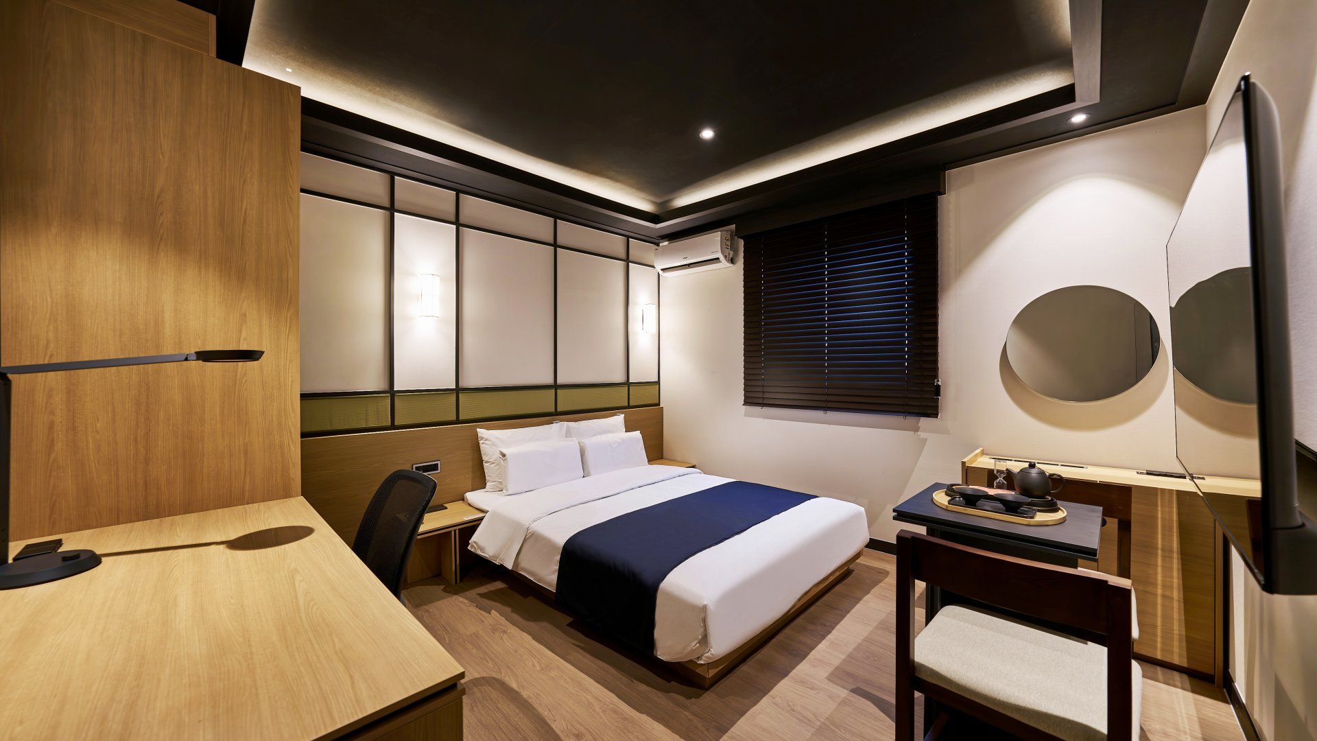 A modern hotel room with a bed, desk, chair, and a wall-mounted TV.