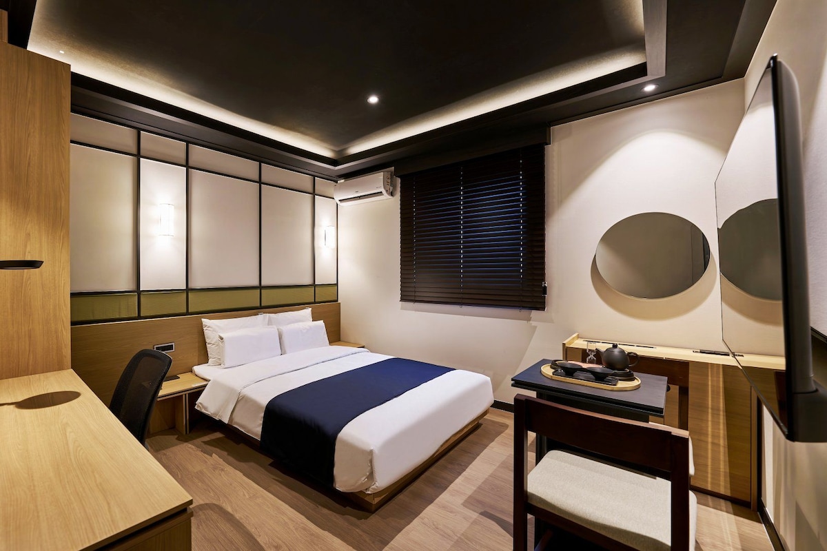 Una habitación de hotel moderna con cama, escritorio, silla y televisor montado en la pared.