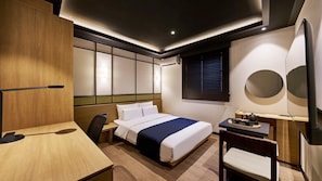 Una habitación de hotel moderna con cama, escritorio, silla y televisor montado en la pared.