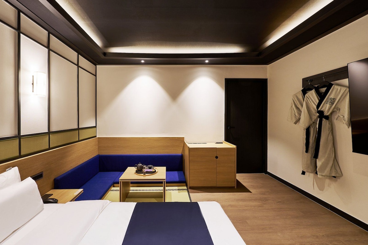 Habitación de hotel con cama, zona de estar, una mesita con tetera y un armario con bata.