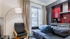 Una sala de estar moderna con un sofá, una butaca, una lámpara de pie y vistas de la ciudad a través de amplios ventanales.