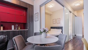 Habitación de hotel moderna con zona de comedor, cama con cabecera blanca y puerta corrediza de vidrio que da a un balcón.