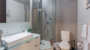 Un baño moderno con ducha envuelta en vidrio, un lavamanos blanco y un inodoro.