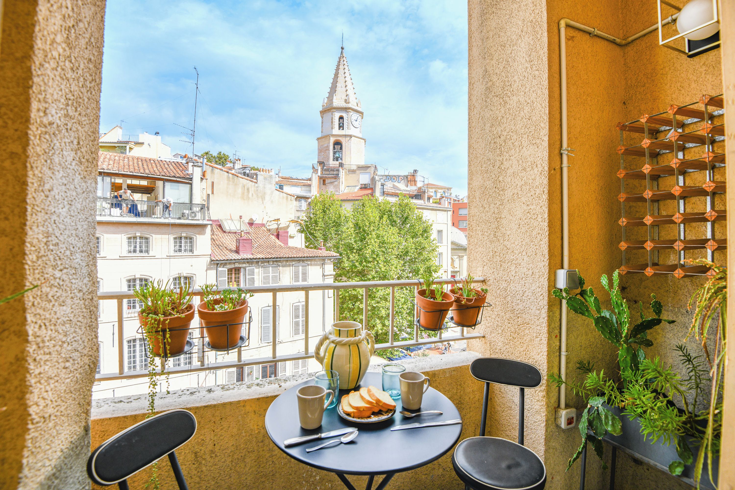 A balcony with a table set for two, potted plants, and a view of a tower.