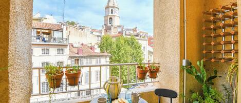 A balcony with a table set for two, potted plants, and a view of a tower.
