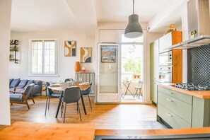 Une cuisine moderne équipée d’une cuisinière à gaz, un coin repas avec une table et des chaises, et un salon avec un canapé et une bibliothèque.