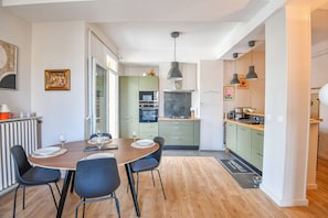 Une cuisine moderne avec des meubles de couleur verte, un coin repas avec une table et des chaises en bois, et un pare-feu noir.