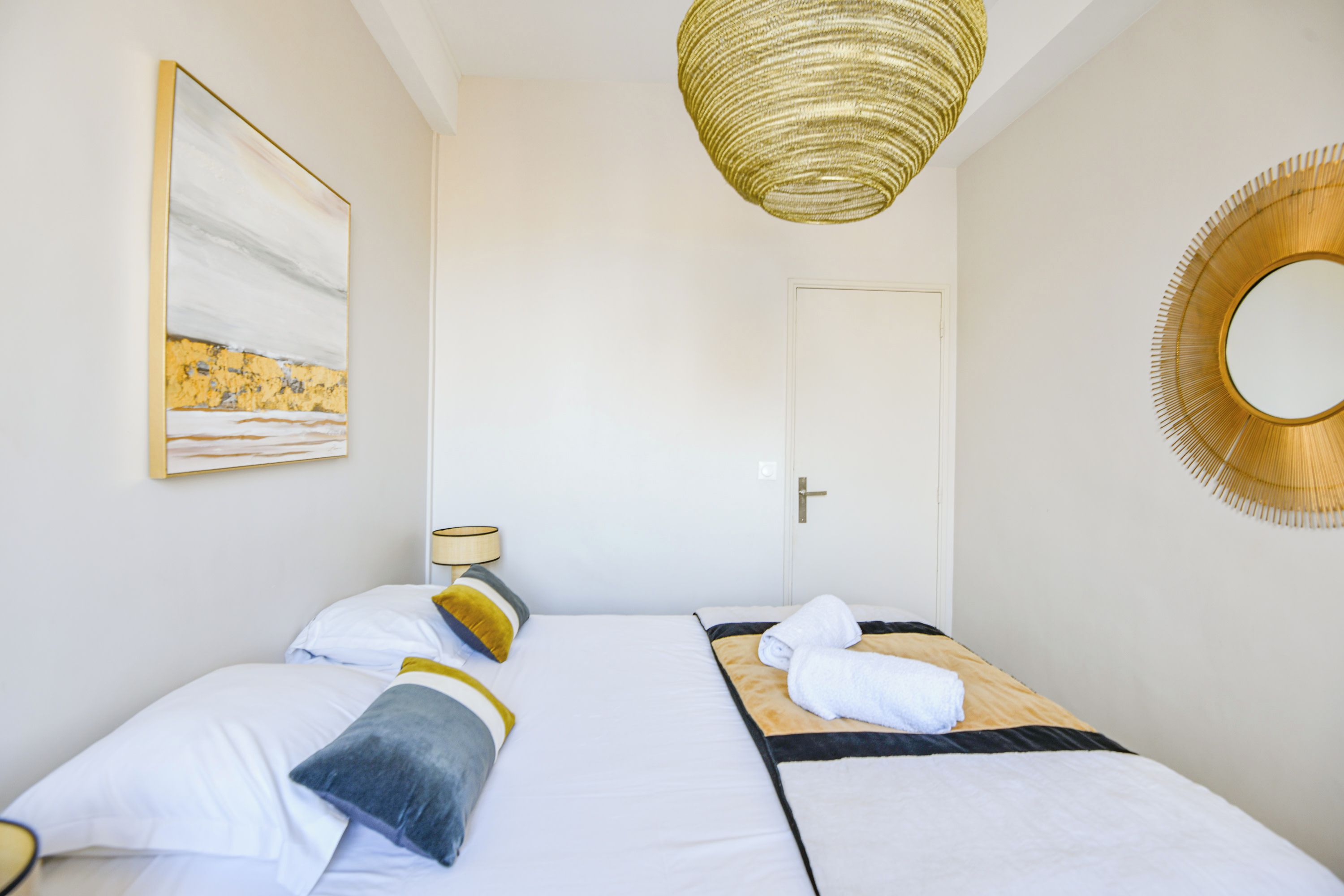 A hotel room with two beds, a painting on the wall, a lamp, and a mirror.