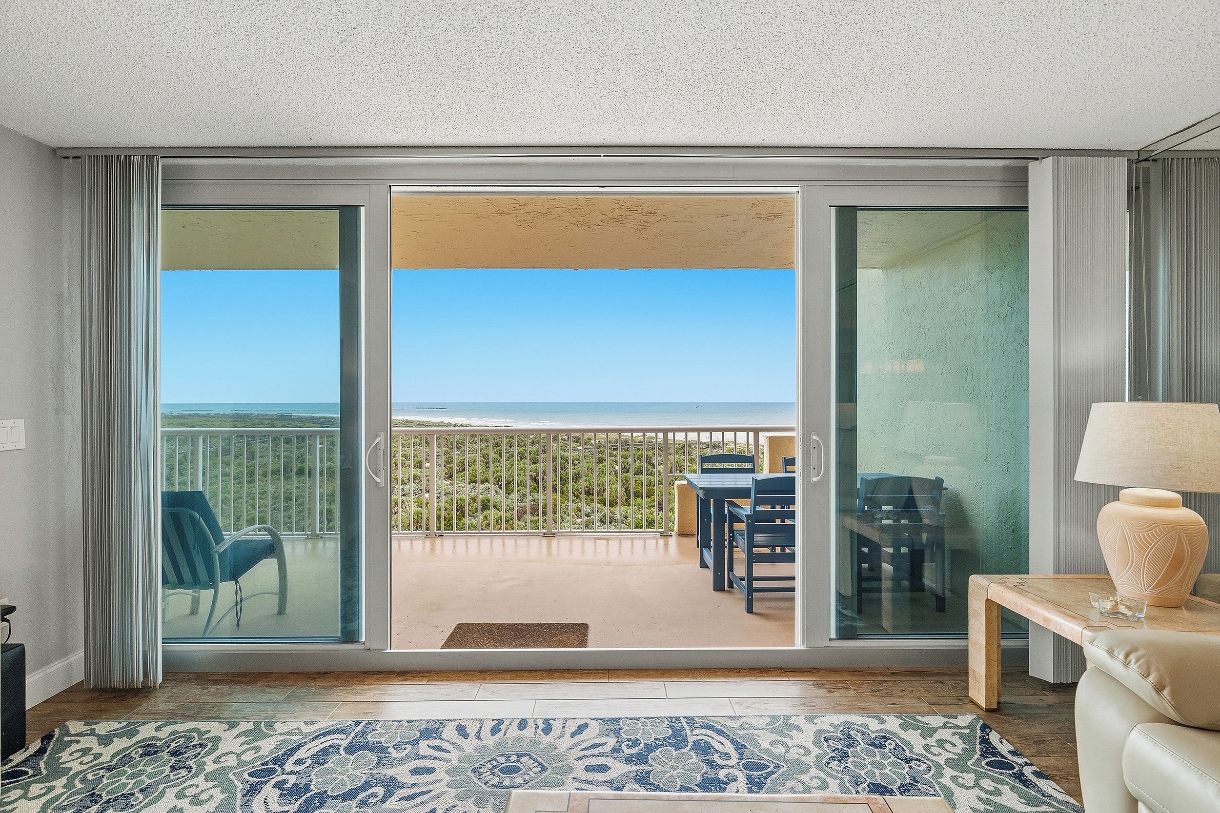 Habitación con vista al océano a través de grandes puertas corredizas de vidrio, un sofá, una mesa y una lámpara.