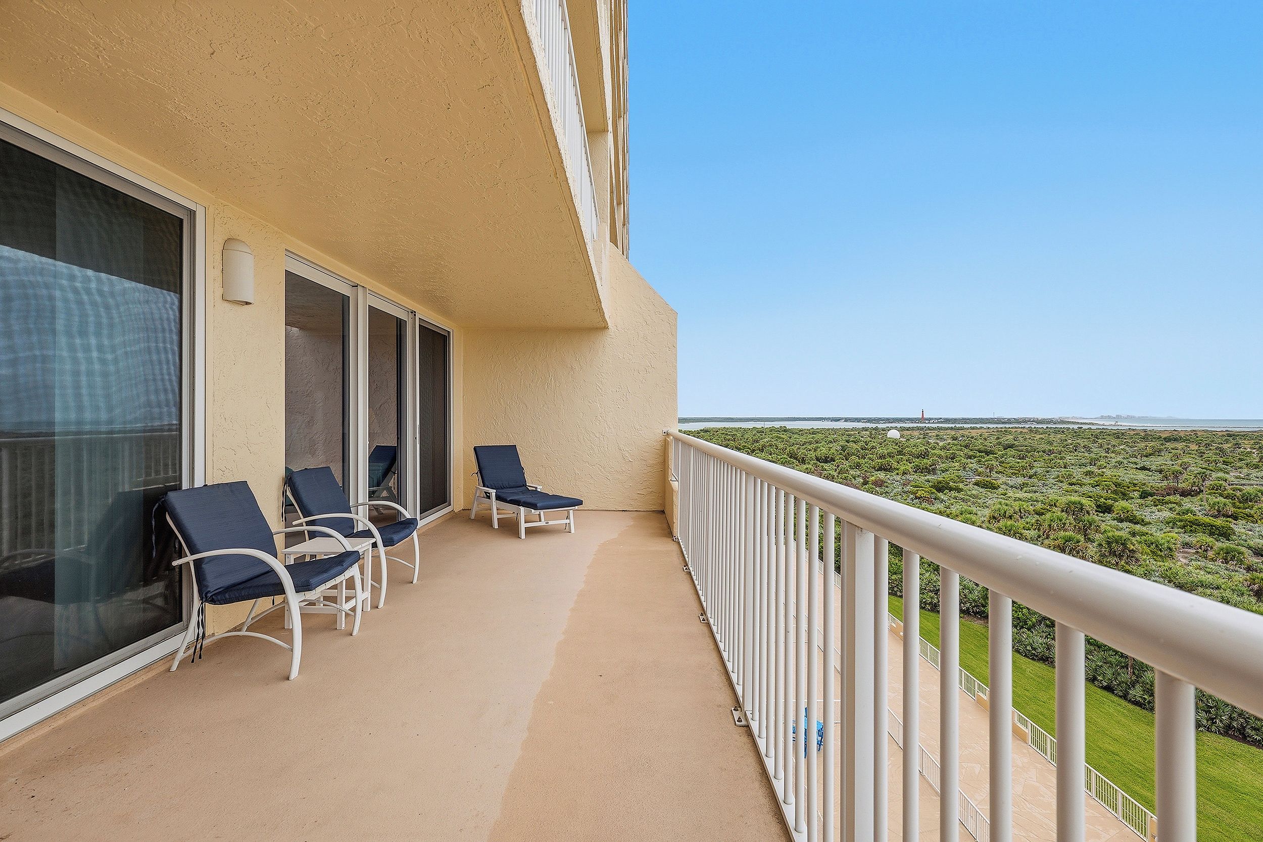 A balcony with two lounge chairs and a table, overlooking a coastal landscape.