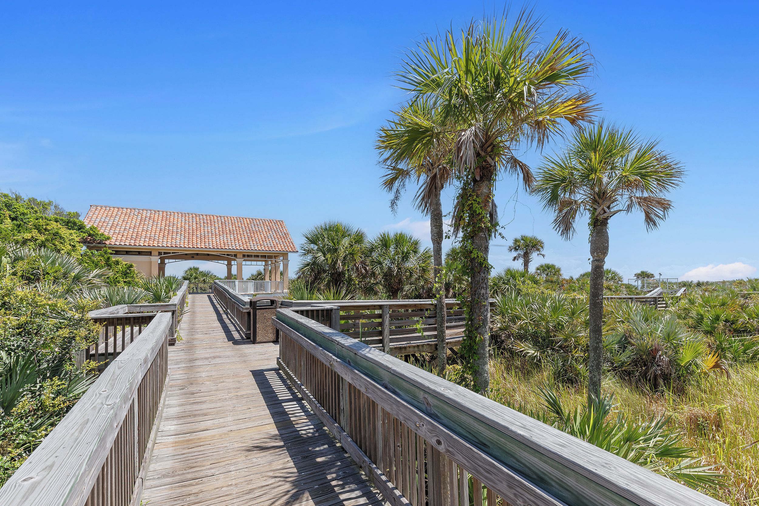 A wooden boardwalk leading to a building with a red-tiled roof.